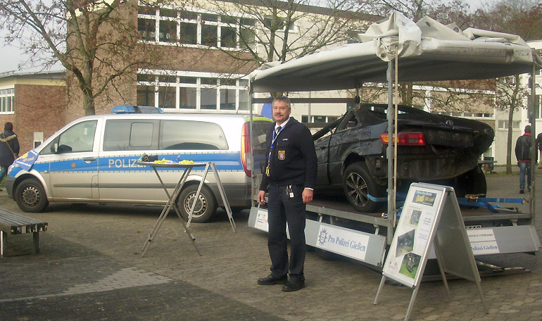 Polizeioberkommissar Steffen Dapper am BOB-Infostand - mit dem Unfallfahrzeug auf dem Schulhof in Grünberg